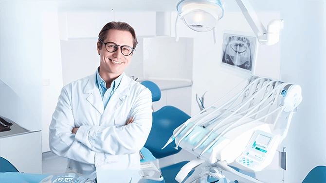 Dentist smiling while standing in front of his dental equipment