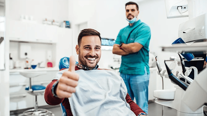 Male patient on dental chair, his hand out with a thumb up