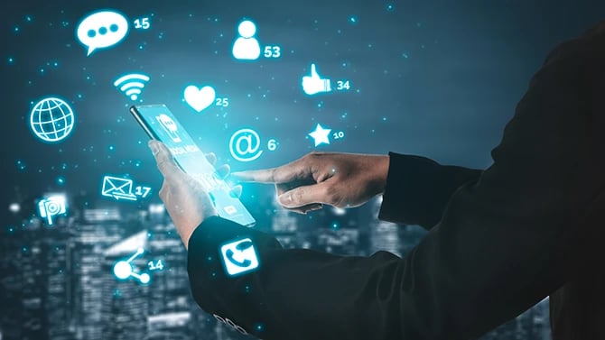 Close up view of hands holding a mobile phone with various lit up icons popping out of the device.