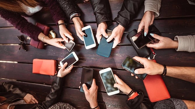 Group of friends holding all their phones forward over middle of the table