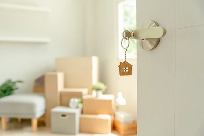 Key inserted into the door of the house, inside the room is a cardboard box containing belongings of a new mover.