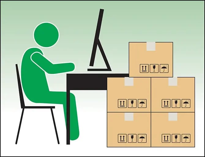 person using a desktop computer with moving boxes stacked beside their desk