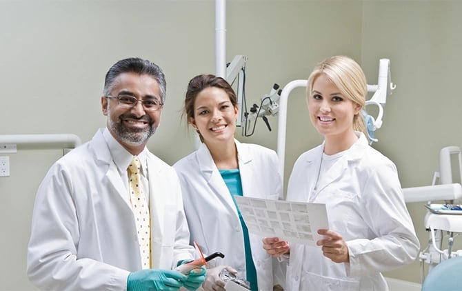 A photo of a dental clinic with three dentists facing the camera, smiling.