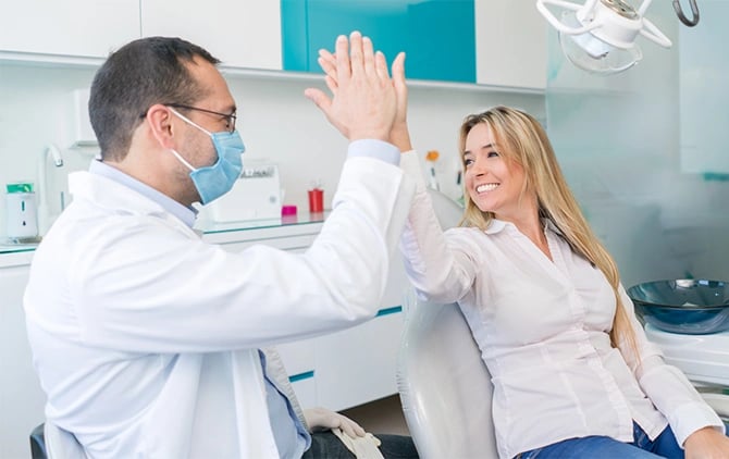 A woman sits in the dental chair giving her dentist a high five