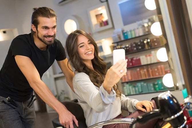  Young woman taking a selfie with her hairdresser after treatment and service.
