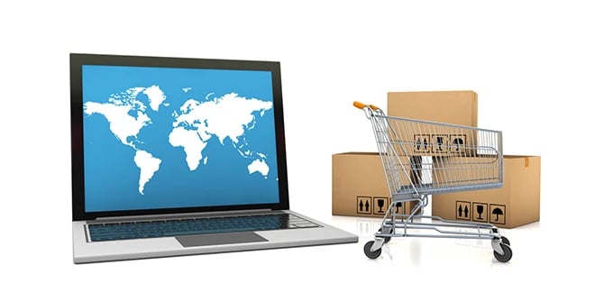 Laptop with a world map and a shopping cart beside boxes to represent online eCommerce.