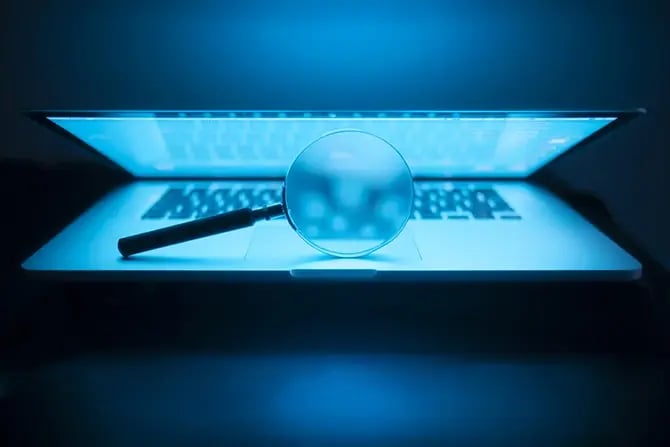 Magnifying glass in the laptop in the dark, illuminated by laptop screen.