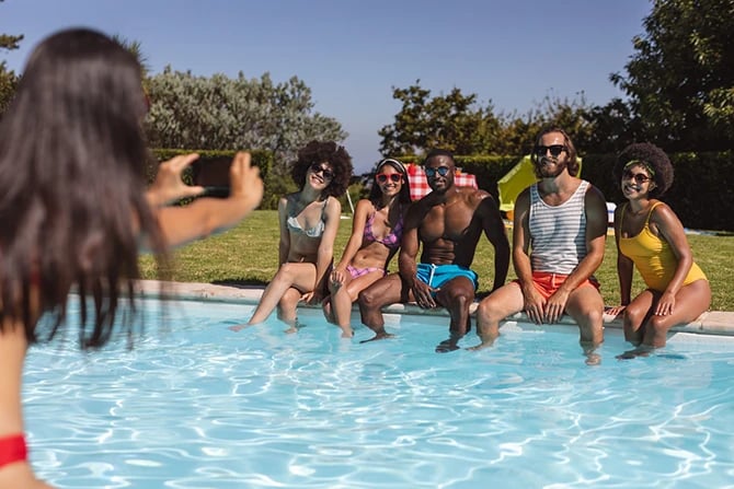Diverse group of friends taking a photo and sitting at the poolside.