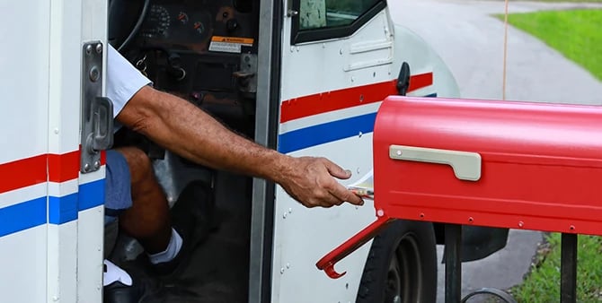 Mailing service mailman reaches out of his truck to deliver direct mail in a mailbox.