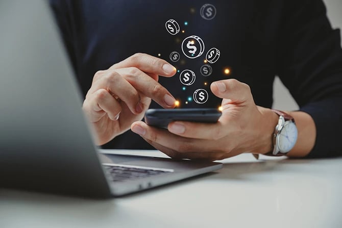 A man's hand using a smartphone with several coin icons.