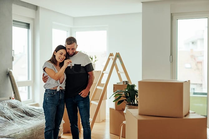 A young couple is standing in their new apartment hugging and holding the keys to their new home.