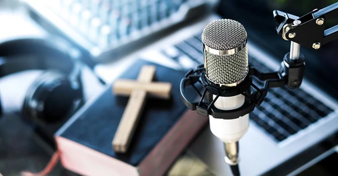 Christian podcast microphone with a cross, a Bible, and a laptop in the background 