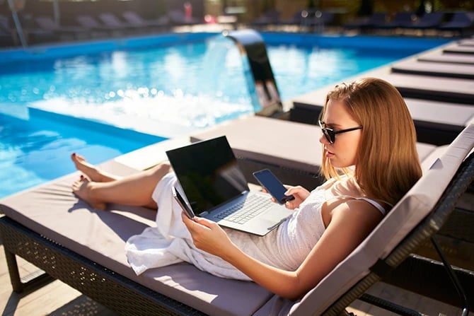Swimming pool owner searching for a pool contractor using her cellphone and laptop near a swimming pool beach bed.