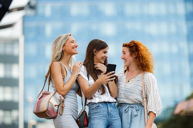 Happy female friends are excited after looking at Facebook Ads or Instagram stories of a beauty salon on a smartphone.