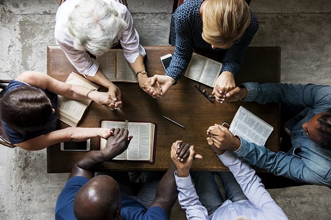 Group of people holding hands around the table while praying