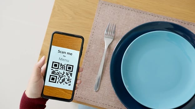 Customer scans QR code for online menu service at table in restaurant.