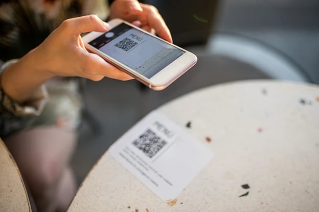 Woman using her mobile phone to scan QR code for an online menu.
